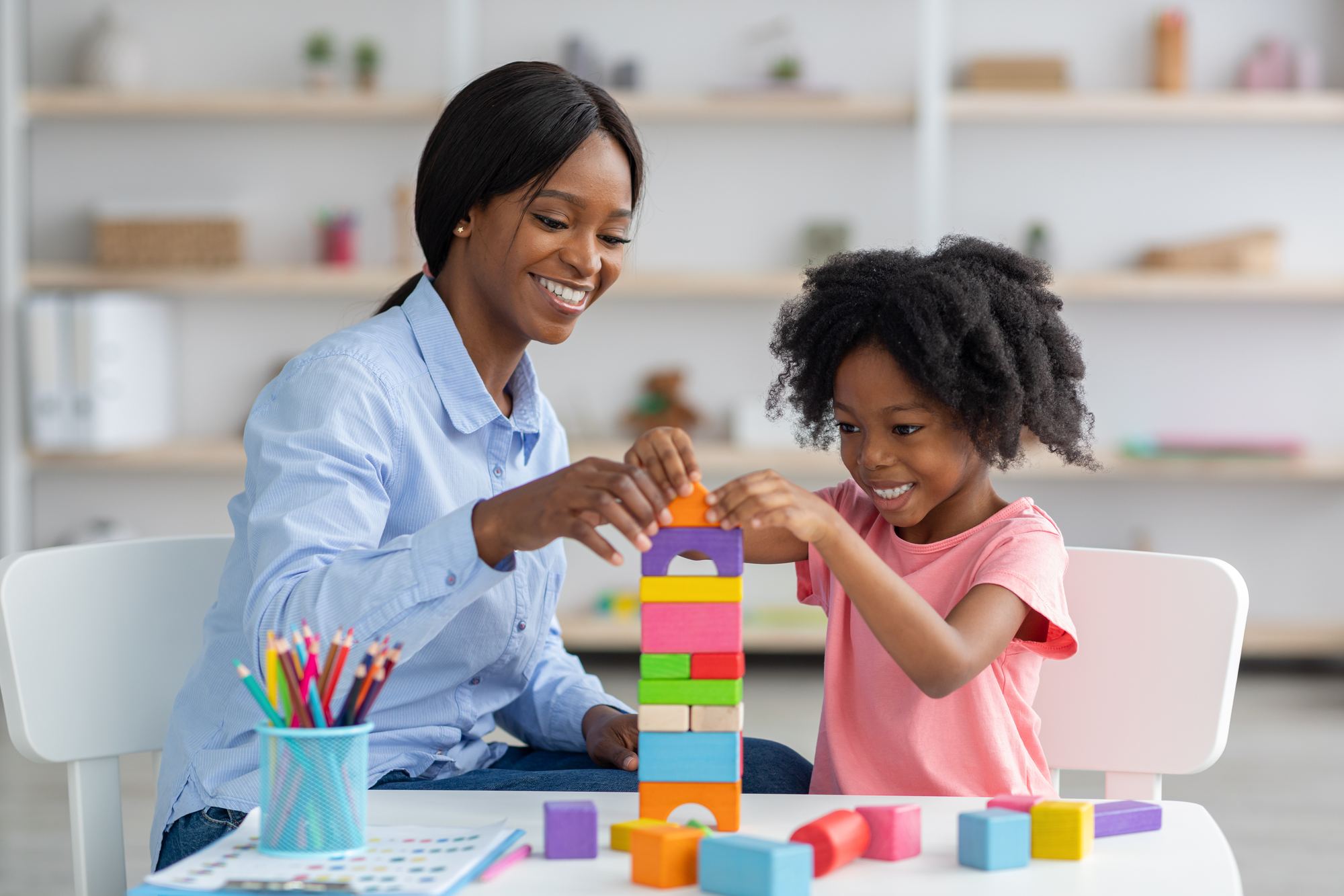 A therapist and a young girl smile as they stack colourful wooden blocks together during a therapy session