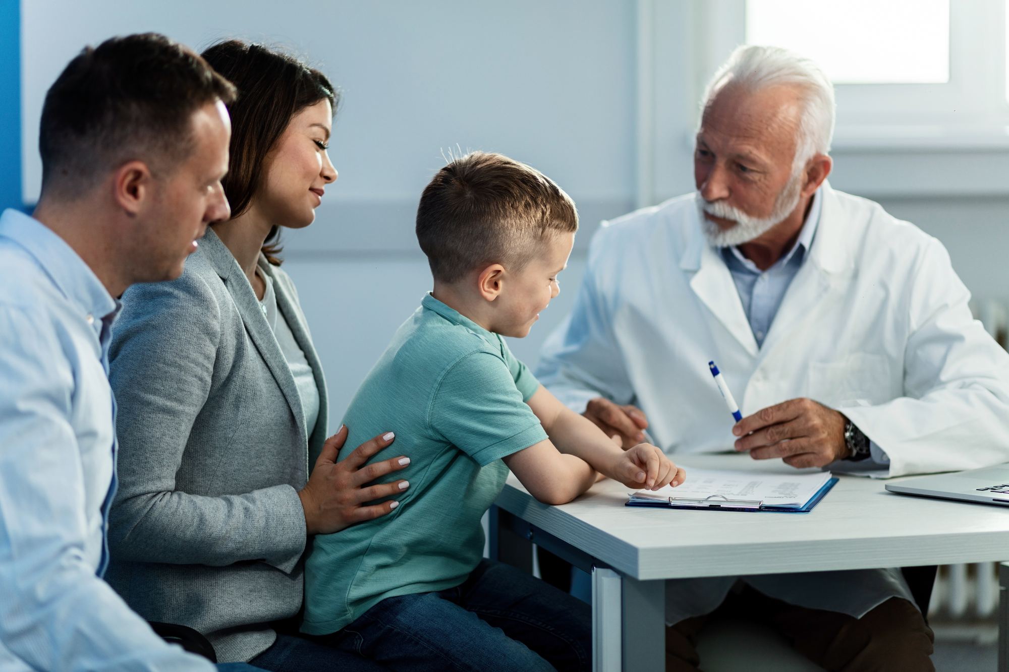 Parents and their young son talk with a doctor across a consultation table